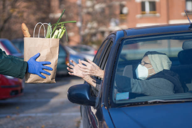 bolsa de papel con suministros esenciales dados a la persona mayor en la cola del punto de distribución de alimentos - begging fotografías e imágenes de stock