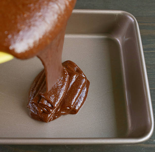 istock Chocolate Cake Batter Being Poured into Greased Cake Pan with Blurry Cake Mixture in Foreground 1299306728