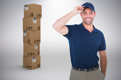 Portrait of happy delivery man wearing cap against grey background