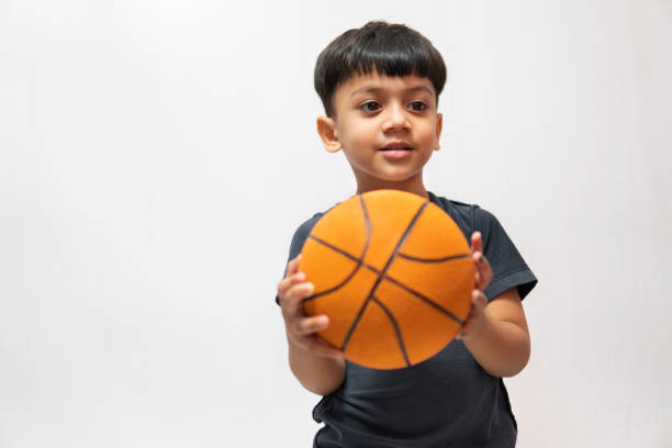 An Asian little boy holding a basketball against white background.