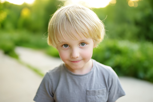 Portrait of a cute green-eyed blonde preschooler boy. Child walking in public park on summer day. Beautiful people.