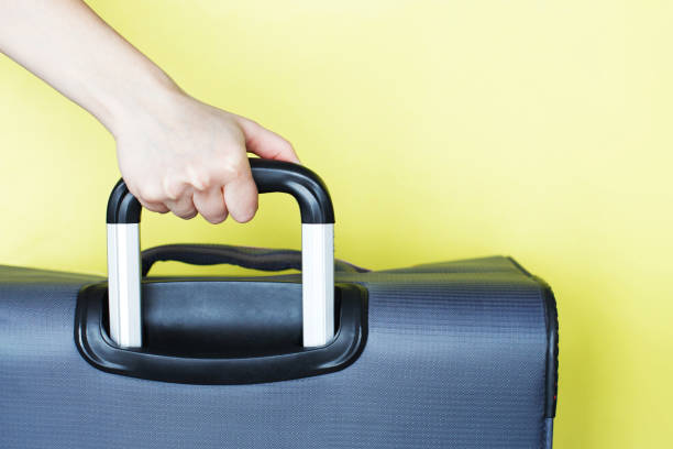istock hand holding a suitcase isolated on a yellow background. Air flight journey concept. Copy space mock up 1299313746