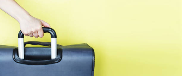 istock hand holding a suitcase isolated on a yellow background. Air flight journey concept. Copy space mock up 1299313801