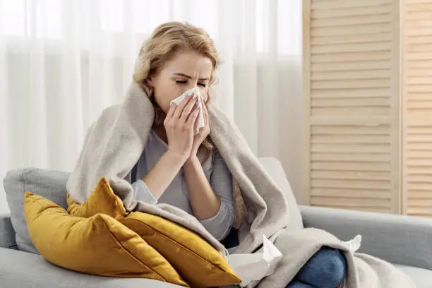 Photo of Ill woman with runny nose sneezes into a napkin