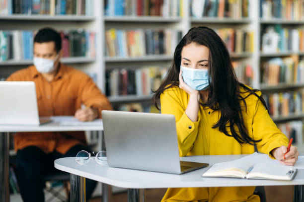 istock Learning during a pandemic. Students sit at a distance from each other with protective masks on their faces. A student girl sits at a desk during a lesson in a medical mask and looks away 1299316620