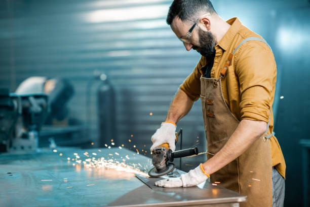 Man working with metal at the workshop Worker dressed in apron doing some metalwork, grinding steel product at the factory. Handsome artisan at the workshop of metal products. High quality photo steel grinding stock pictures, royalty-free photos & images