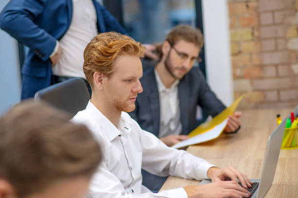 istock Redhaired man working at laptop and colleague managers 1299319672