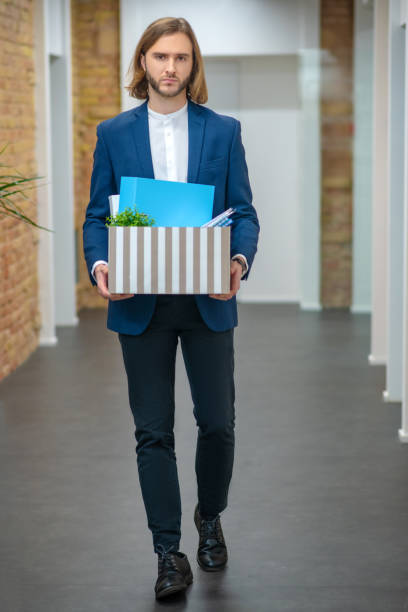 istock Young unhappy man in suit with box 1299319700