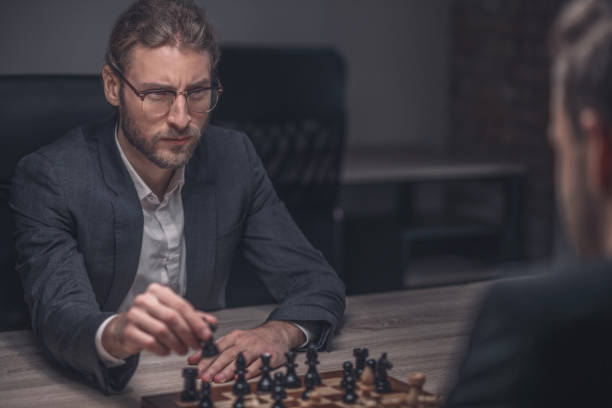 istock Young man with glasses making chess move 1299319808