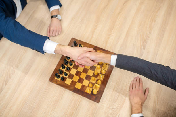 istock Hands of two men in handshake over chessboard 1299319846