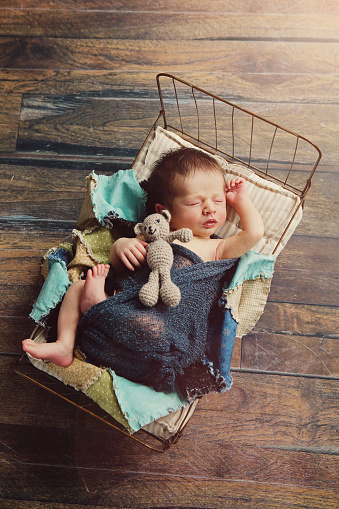 A newborn baby sleeping in a tiny bed, clutching a small teddy bear.