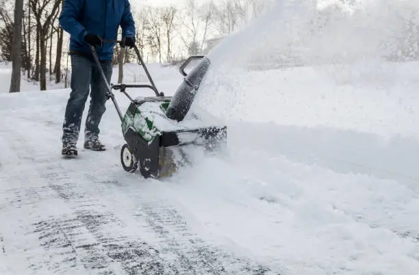 Snow blower in action clearing a residential driveway after snow storm.  Snow removal, winter snow storm, weather concept.