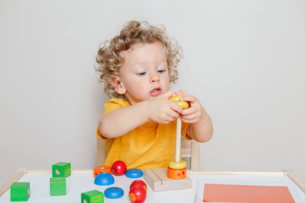 istock Cute baby toddler playing with learning toy pyramid stacking blocks at home or kindergarten. Early age education. Kids hand brain fun development activity for preschoolers. 1299323066
