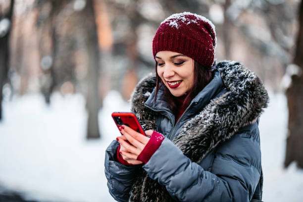 istock Beautiful woman in snowy park checking phone messages 1299323493