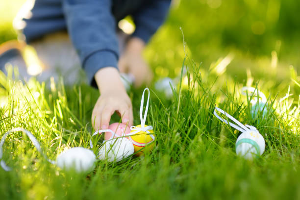 Cute little boy hunting for colorful eggs in spring garden on Easter day. Focus on eggs. Traditional entertainment for kids during easter festival outdoors.