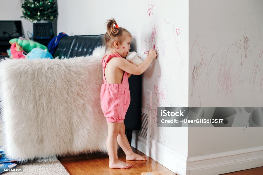 Funny cute baby girl drawing with marker on wall at home. Toddler girl child with milk bottle playing at home. Authentic candid childhood lifestyle moment. Young artist painting on wall at living room Funny cute baby girl drawing with marker on wall at home. Toddler girl child with milk bottle playing at home. Authentic candid childhood lifestyle moment. Young artist painting on wall in living room Child Stock Photo