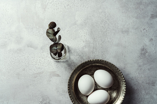 White eggs in metal bowl with eucalyptus leaf on grey background.  Ester eggs. Shot from directly above.