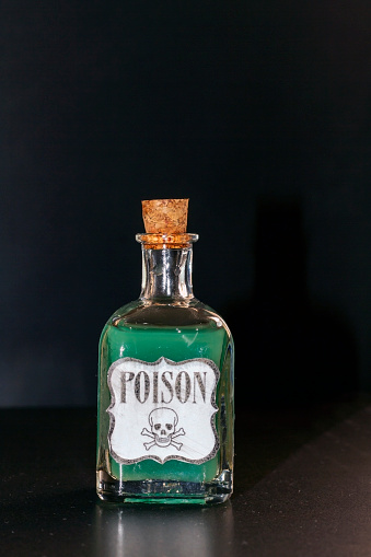 Concept of toxic thing. Transparent bottle with green liquid simulating poison. The label reads poison along with a skull and two tibias