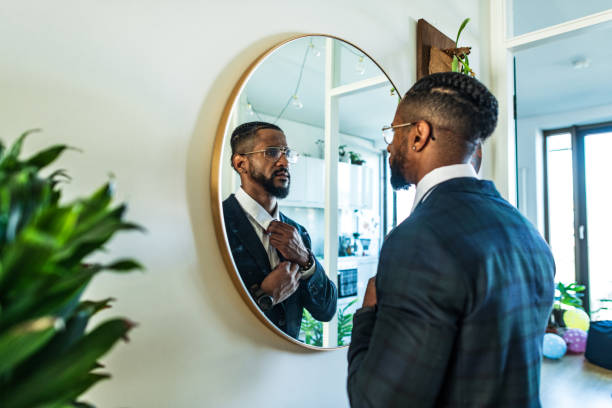 Businessman preparing for a big  day at work Young man at his home ties the tie in front of the mirror looking in mirror stock pictures, royalty-free photos & images