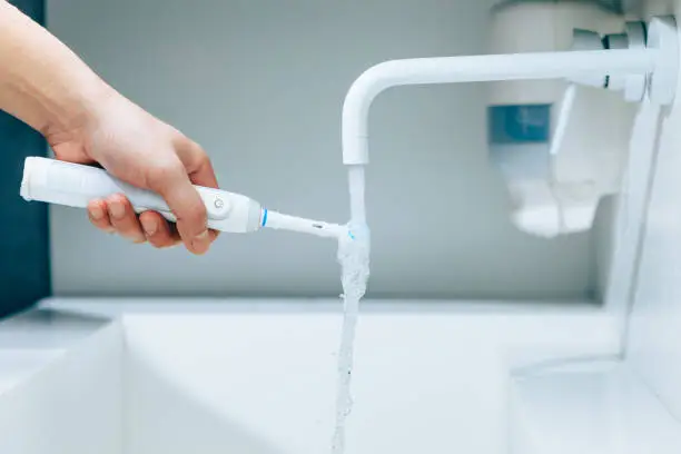 hand holding a toothbrush under flowing water from faucet in a bathroom, close-up view