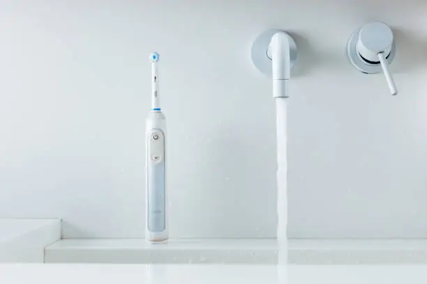 electric toothbrush on a wash-bowl, water flowing from faucet