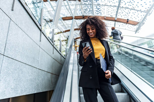 Businesswoman uses phone in public Portrait of young business woman on a escalator banking stock pictures, royalty-free photos & images