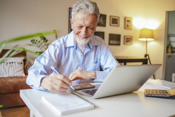 istock Senior man using a laptop at the table in the living room 1299334096