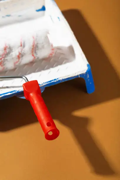 Blue tray paint and red paint roller against a brown background
