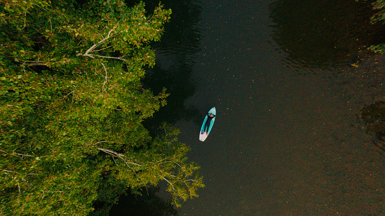 High angle photo of a senior triathlete lying on the paddleboard and relaxing after paddleboarding on the river, as a part of his triathlon training.