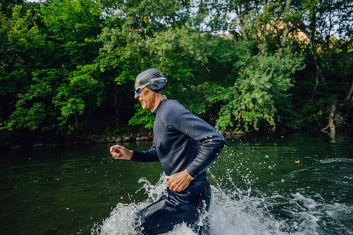 Photo of a senior triathlete running into the river, preparing for swimming, as a part of a triathlon training.