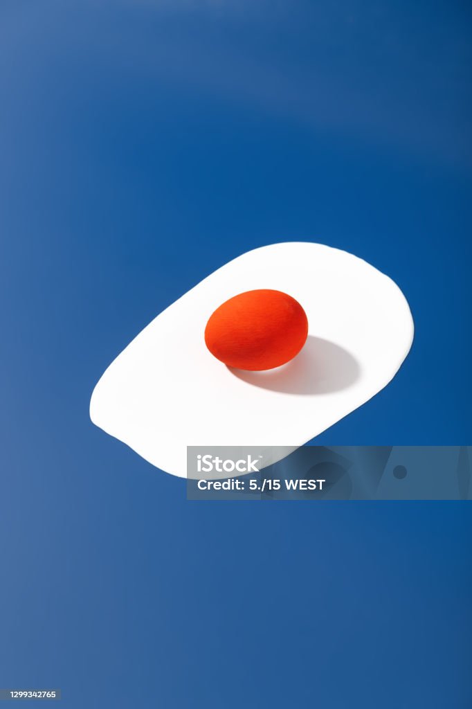 Red egg in white paint on a blue b ackground. Concept fried egg top view Blank Stock Photo