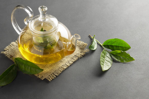 istock Green tea in glass teapot with fresh tea leaves on rustic table, hot drink concept 1299342805