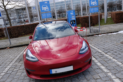 Munich, Germany Bavaria - January 29, 2021: Tesla Motors red electric vehicle (ev) car parked at a charging station parking lot.