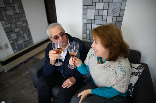 Senior men and senior woman sitting on sofa in living room and drniking wine