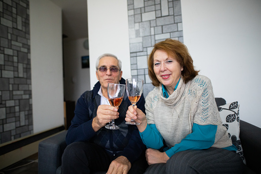 Senior men and senior woman sitting on sofa in living room and drniking wine