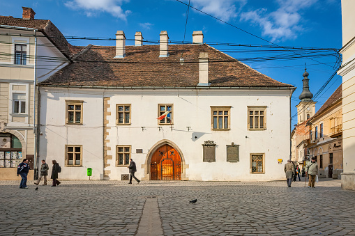 Pedestrians walk in front of the 15th century landmark house, where Matthias Corvinus, King of Hungary, was born, in downtown Cluj Napoca, Romania on a sunny day.