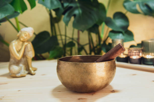 istock Tibetan singing bowl with special stick, burning candles and Golden Buddha decorative statuette on the wooden table with green plants background. Meditation and Relax. Exotic massage. Selective focus 1299349892