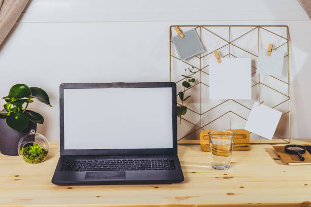 istock Modern workplace - wooden desk with laptop mockup white empty screen, mood board with pined notes and photo, green plants at work space in home office room interior. Selective focus. 1299349894