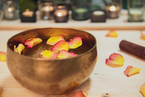 Tibetan singing bowl with floating in water flower petals. Special sticks, burning candles, petals on the wooden background. Meditation and Relax treatment. Exotic massage. Selective focus.