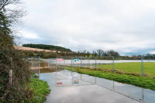 Photo of Flood protection works with signs and fences on the overflowed river's banks due to heavy rain on the east England countryside. Selective focus, copy space.