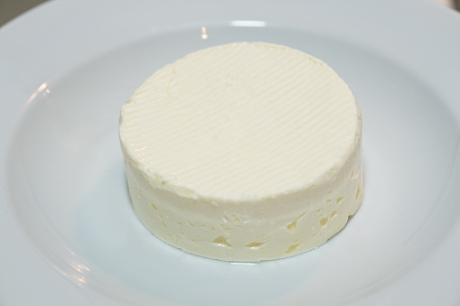 Feta cheese in a white plate, round block of soft cheese