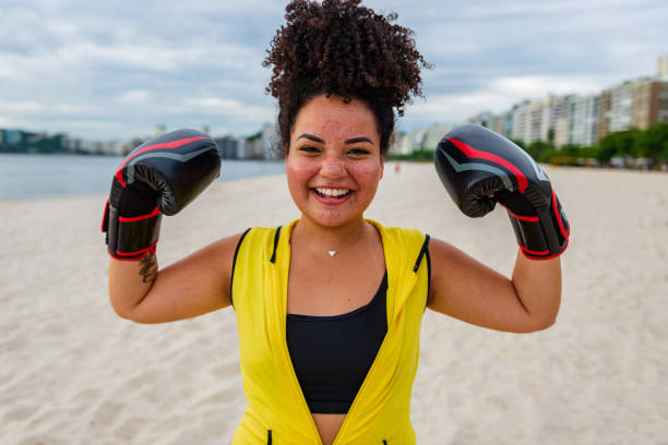 Confident chubby young athlete in sportswear Happy Brazilian woman with boxing gloves on the beach women boxing sport exercising stock pictures, royalty-free photos & images