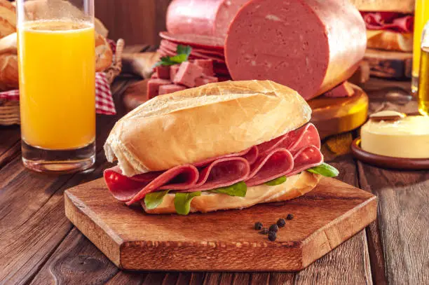 Mortadella sandwich with orange juice, butter and piece of mortadella on wood background