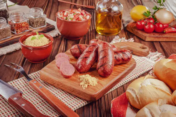 Grilled brazilian sausages on the wooden board with bread, salad, farofa and ingredients - Linguiça churrasco