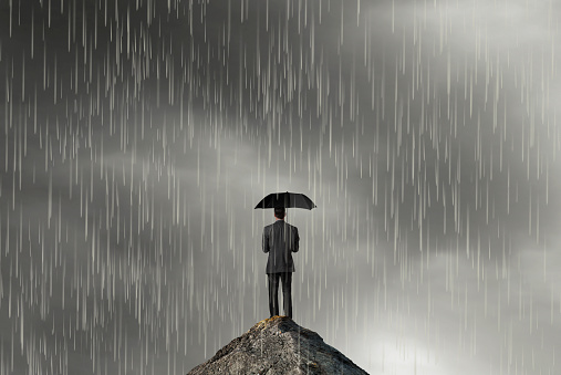 A man holds an umbrella as he stands on a mountain top in a rain storm.