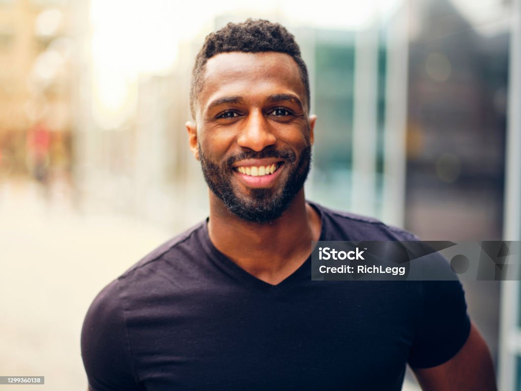 Fit Man Standing Outdoors in a City A fit black man with a beard, standing outdoors in a city area. Men Stock Photo