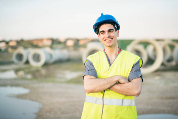istock Posing young worker in factory outdoors, smiling with arms crossed 1299364122