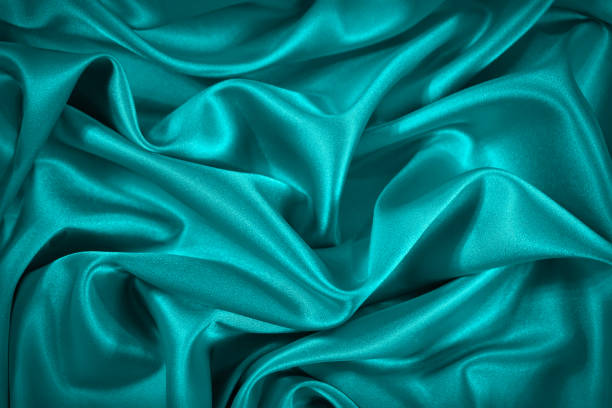 istock Blue and green silk satin fabric. Elegant teal color background. Liquid wave or silk soft wavy folds. 1299366547