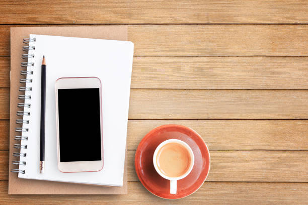 istock Flat lay-Empty blank paper notebook and smart phone on brown wooden table background 1299375506