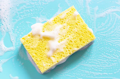 Yellow sponge with foam on a blue background close up.